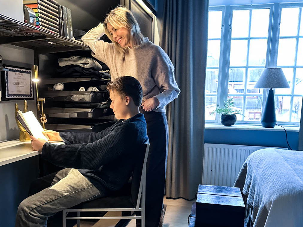 En pojke läser en bok vid ett skrivbord från Elfa medan hans mamma ser på.