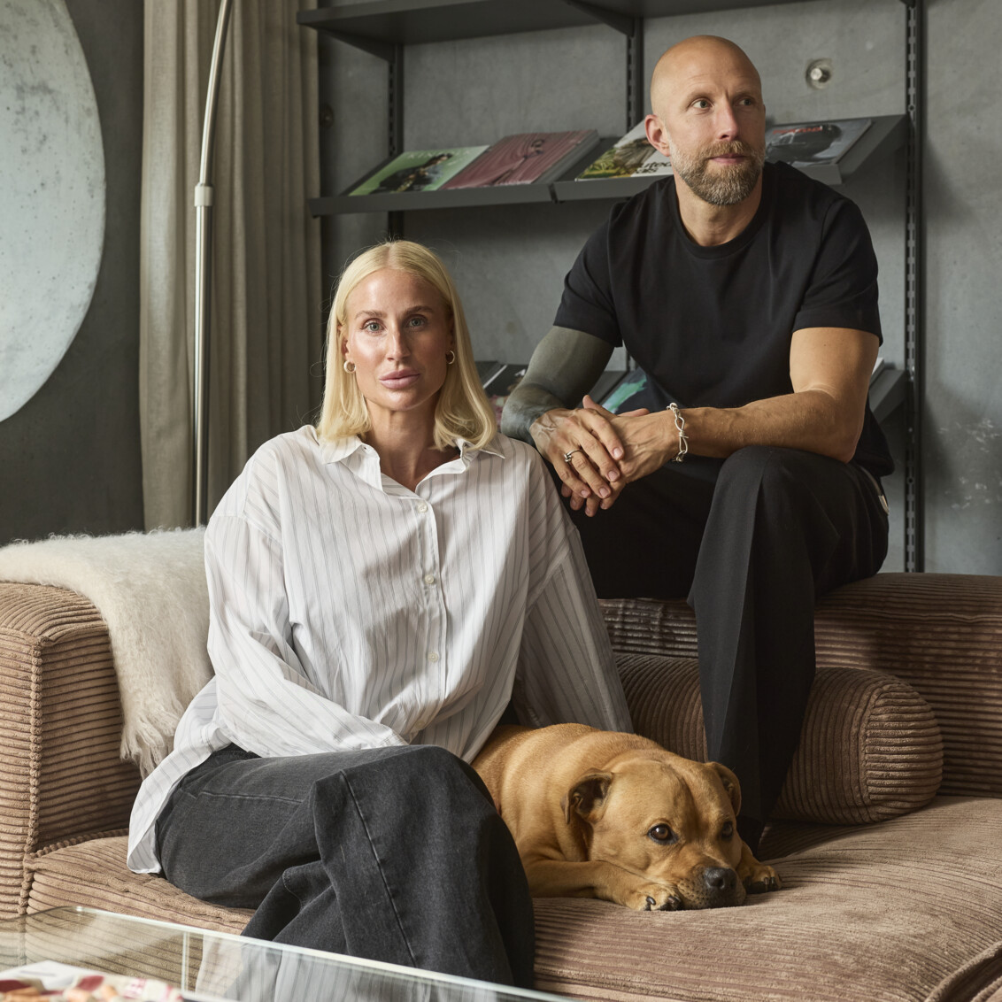 Emma och Linus sitter i soffan i sitt vardagsrum med hyllor i grått från Elfa med böcker.