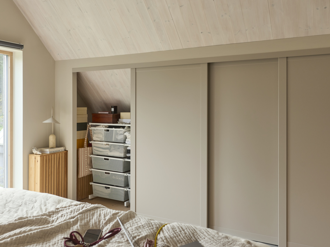 Sovrum med Elfa garderob som har fristående förvaring och skjutdörrarna Grace med fyllningarna sandbeige och spegel.