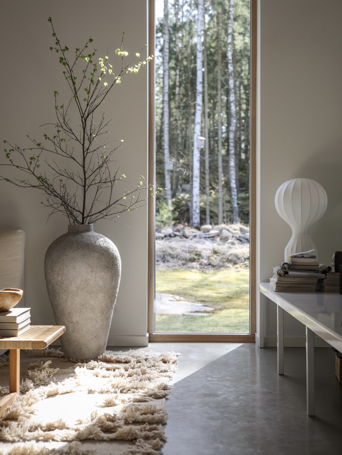 En stor vas med björkris vid ett fönster som vetter mot en skog.