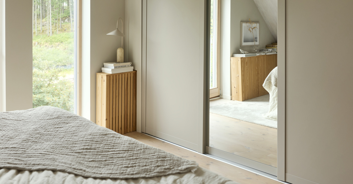 Sovrum med Elfa garderob som har skjutdörrarna Grace med fyllningarna sandbeige och spegel.