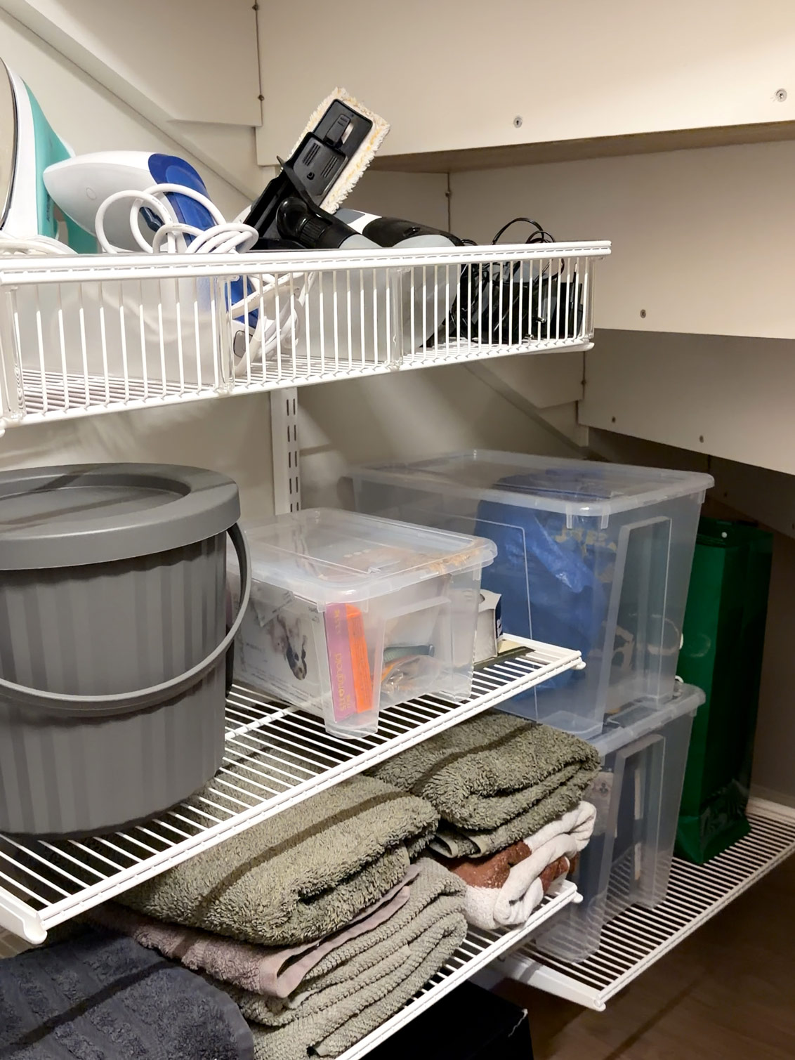 Elfa hyllor under en trappa med städprodukter.