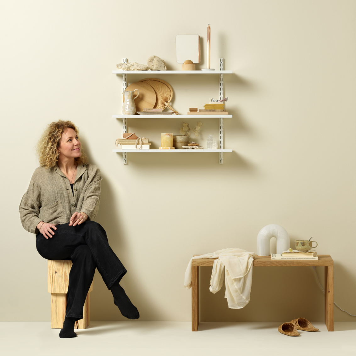 Daniella istuu valkoisen Sparring by Elfa plug-in -hyllypakkauksen vieressä, jossa on vaaleita koristeita. 