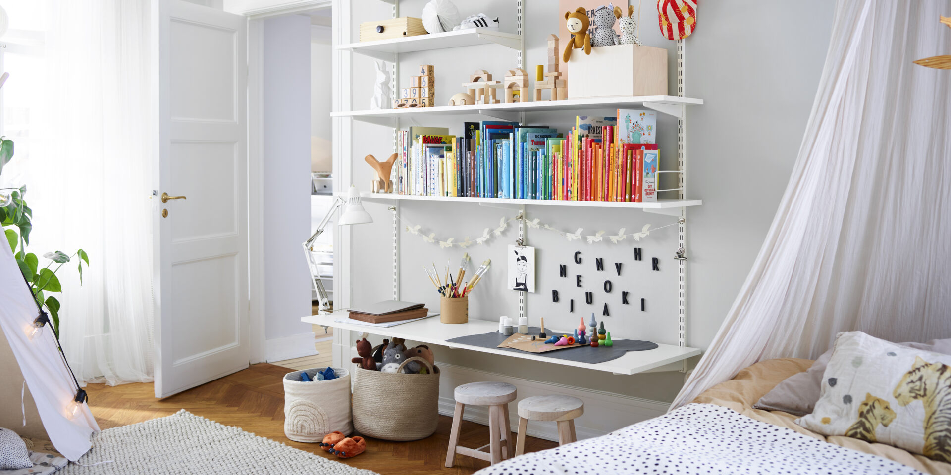Pokój dziecięcy z półką pełną książek Sparring by Elfa w kolorze białym, z dolną półką pełniącą funkcję biurka.