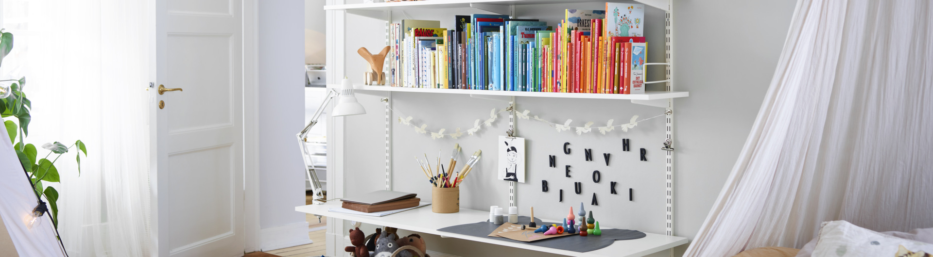 Pokój dziecięcy z półką pełną książek Sparring by Elfa w kolorze białym, z dolną półką pełniącą funkcję biurka.