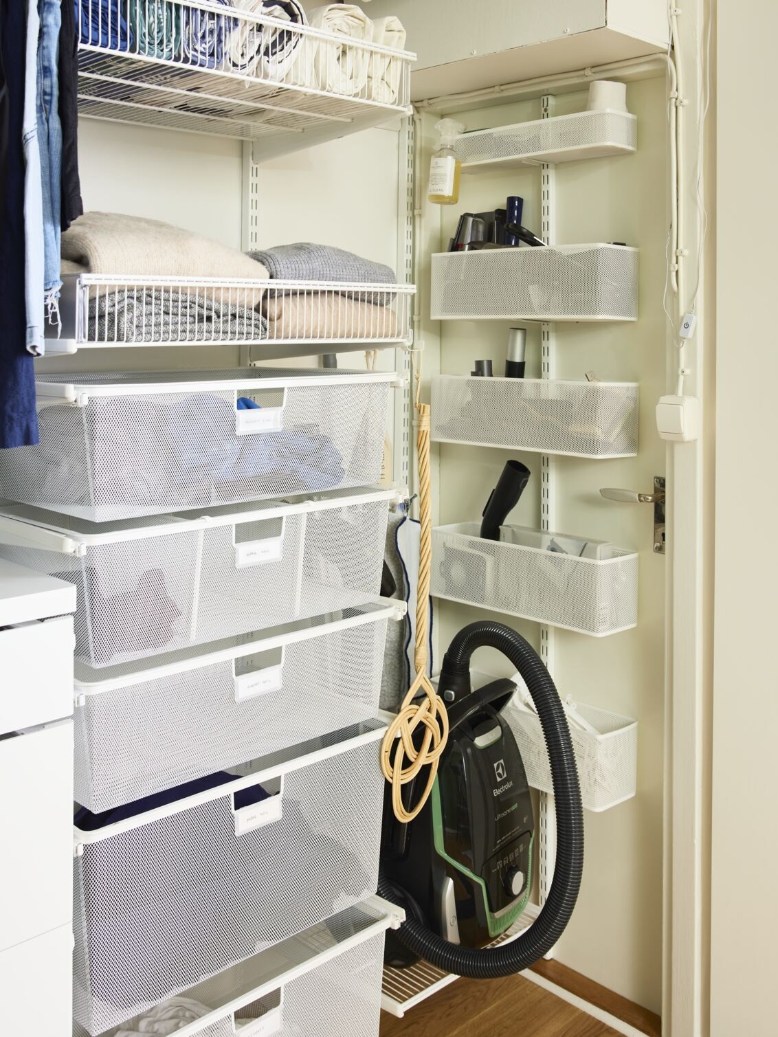 Ett hörn med Elfa förvaring med trådhyllkorgar, meshbackar och meshkorgar där det förvaras kläder och städsaker.