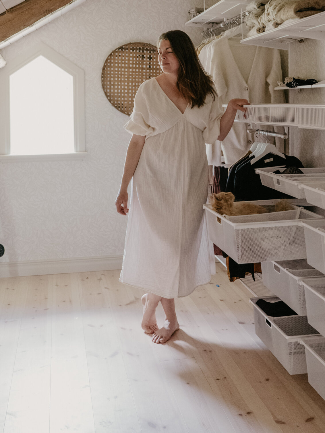 En kvinna hänger byxor på en byxhängare i en öppen garderob från Classic by Elfa i vitt.