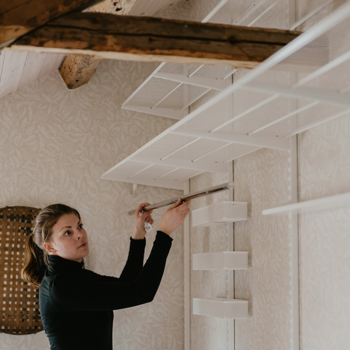 Johanna Berglund monterar Classic by Elfa förvaring i vitt på en vind med takbjälkar.