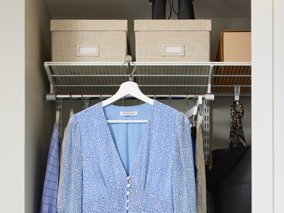 Biała szafa Classic by Elfa z rozsuwanym drążkiem na ubrania, na którym wisi niebieska sukienka.
