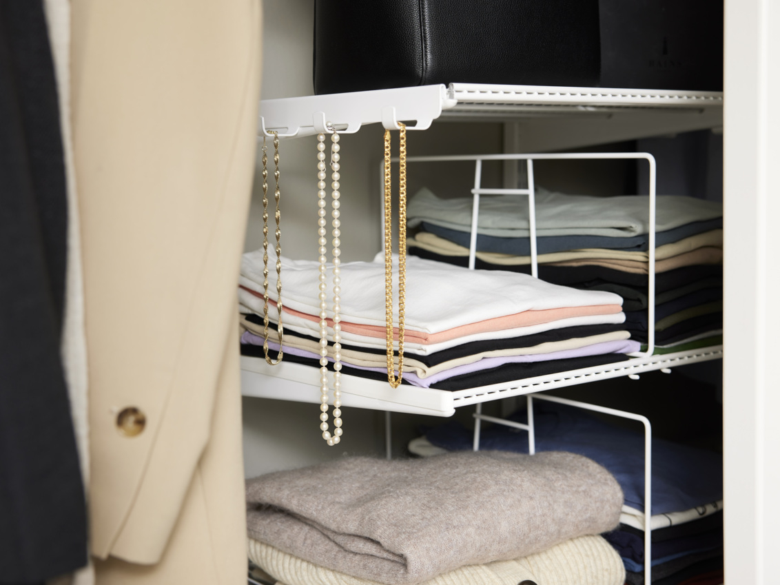 Biała szafa Classic by Elfa z wieszakiem bocznym na złotą biżuterię i naszyjnikiem z perłami.