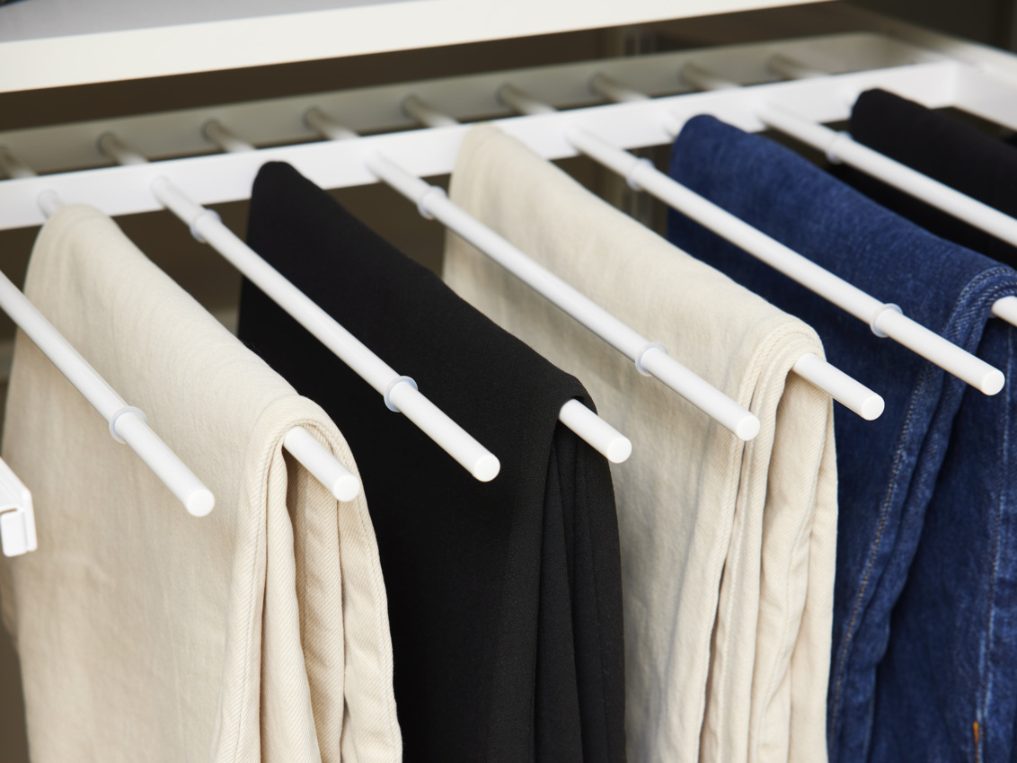 Wyciągany wieszak na spodnie Classic by Elfa w kolorze białym, na którym można zawiesić spodnie w kolorze beżowym i czarnym oraz dżinsy.