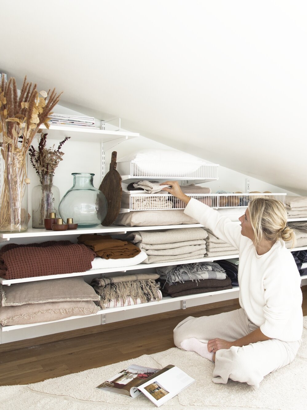 Niki Brantmark sitter på golvet på en vind med förvaring från Classic by Elfa under snedtak.