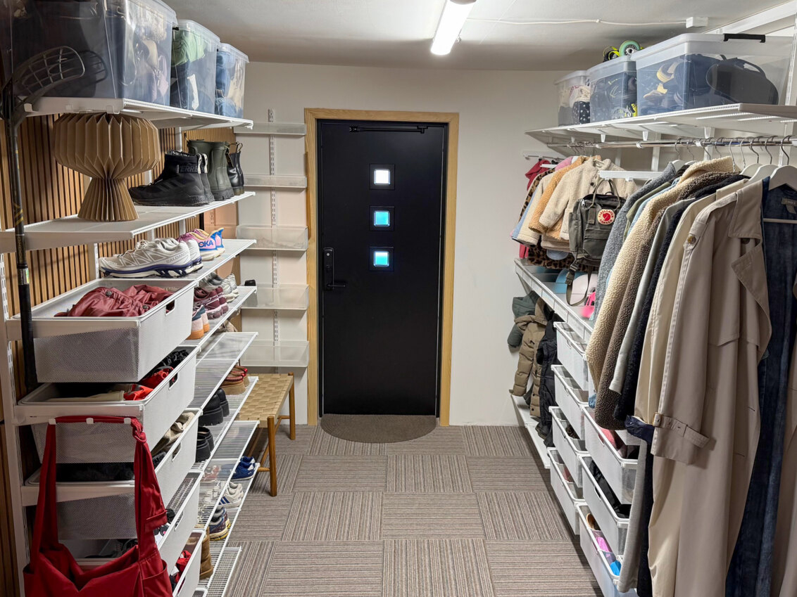 Hall med garderober från Classic by Elfa på två av väggarna fyllda med ytterkläder och skor.