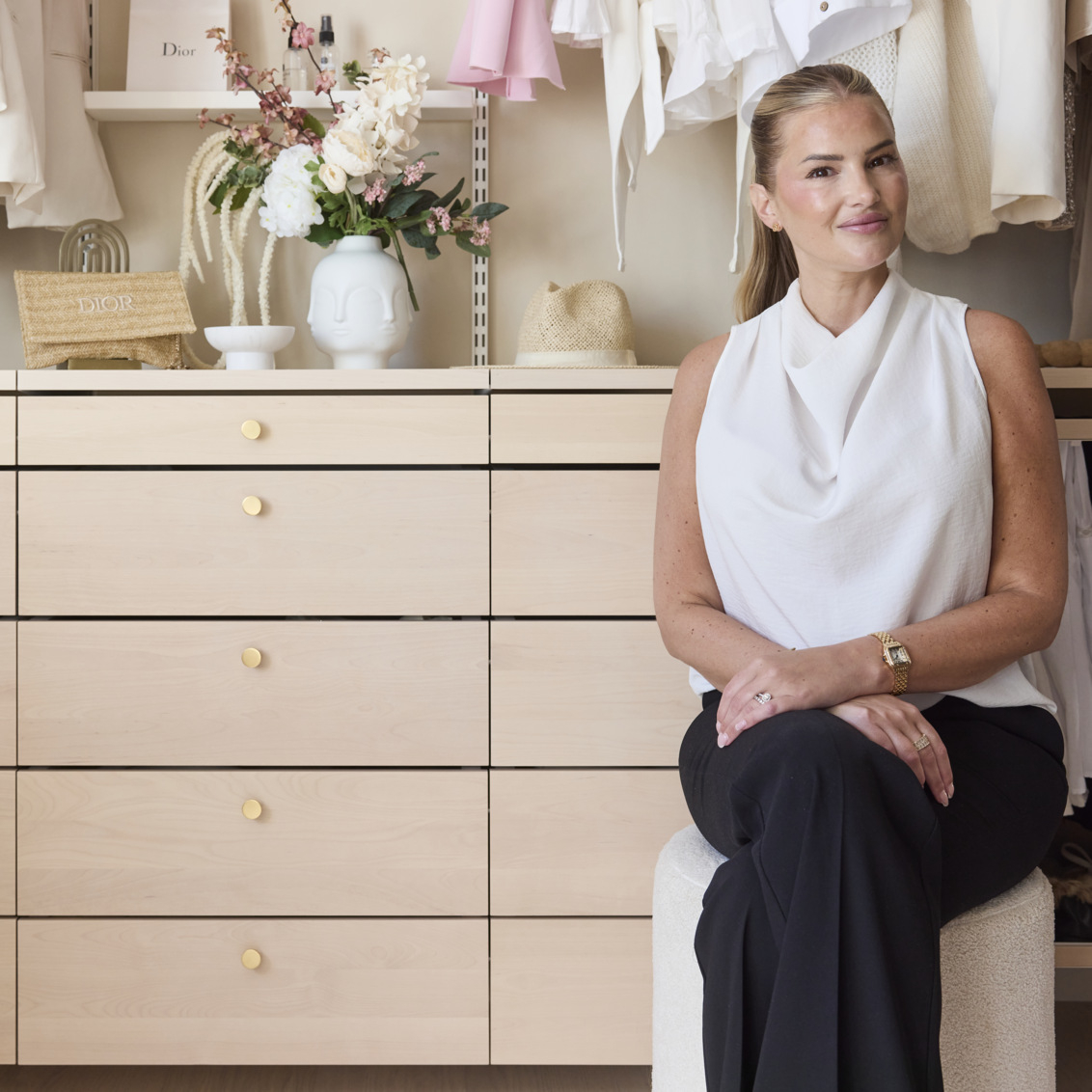 Ida-Marie is sitting by an open wardrobe from Décor+ by Elfa in white and birch.