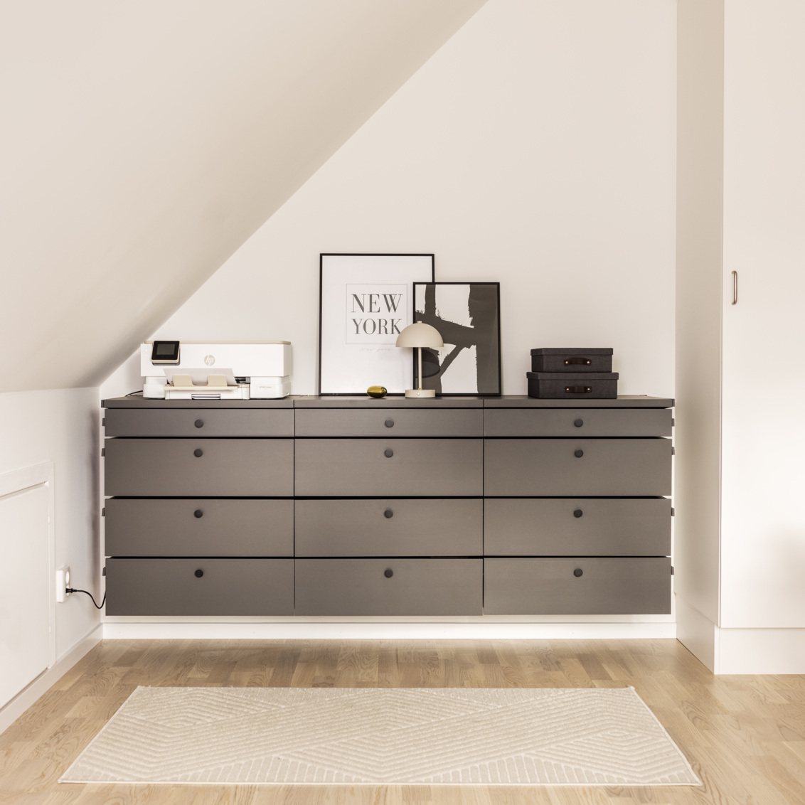 Byrå från Décor+ by Elfa i grått med prydnader ovanpå under ett snedtak.