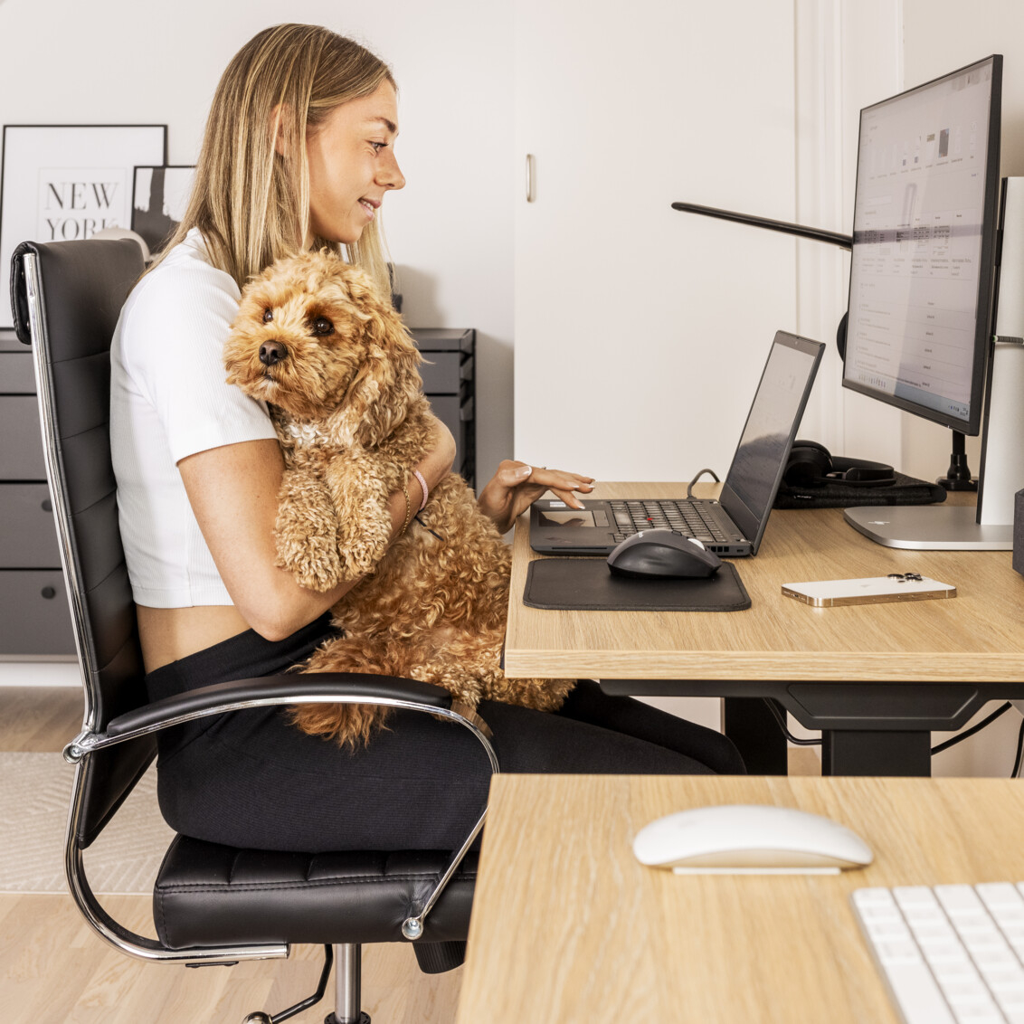 Lisa Lilja sitter med sin hund vid datorn i ett hemmakontor med ett sideboard från Décor+ by Elfa med lådor i grått.