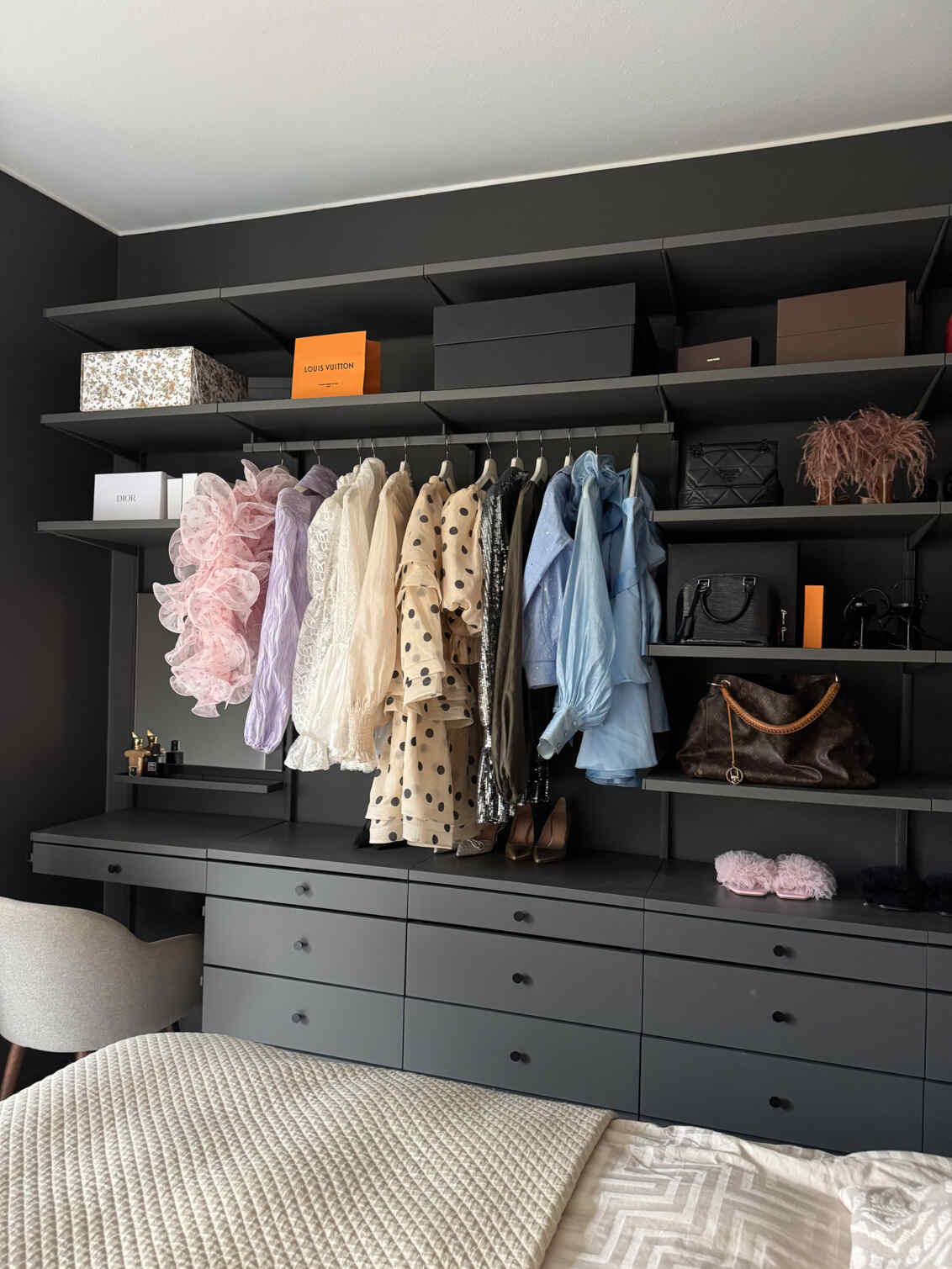 Ett sovrum med förvaring från Décor+ by Elfa i grått med hängande kläder och solida lådor.
