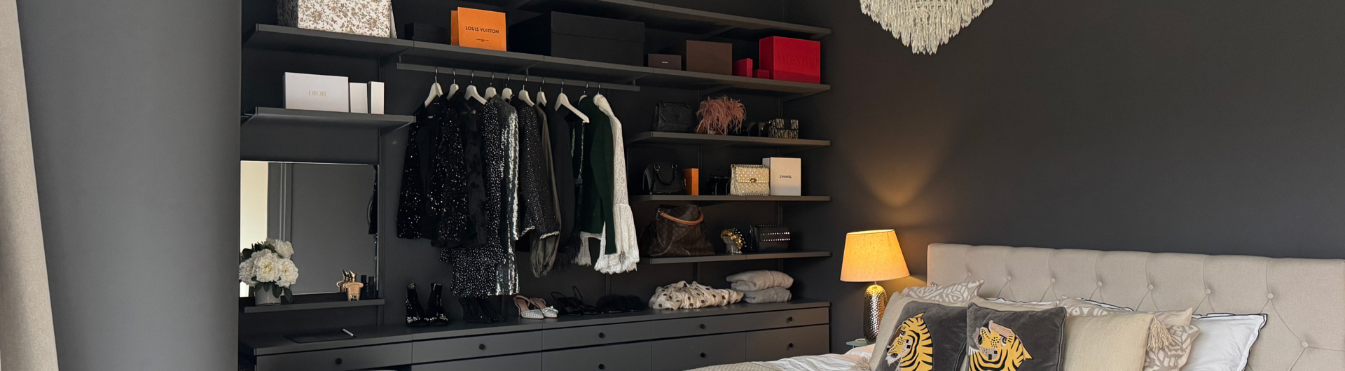 Ett sovrum med förvaring från Décor+ by Elfa i grått med hängande kläder och solida lådor.