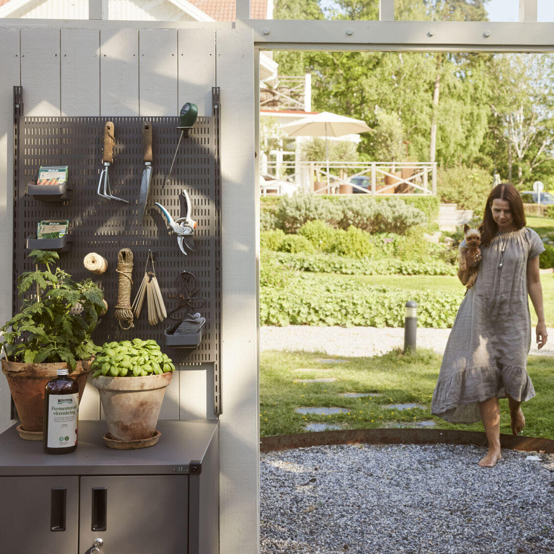 Carin på väg in i växthuset där det finns en Garage+ förvaringstavla från Elfa med trädgårdsredskap.