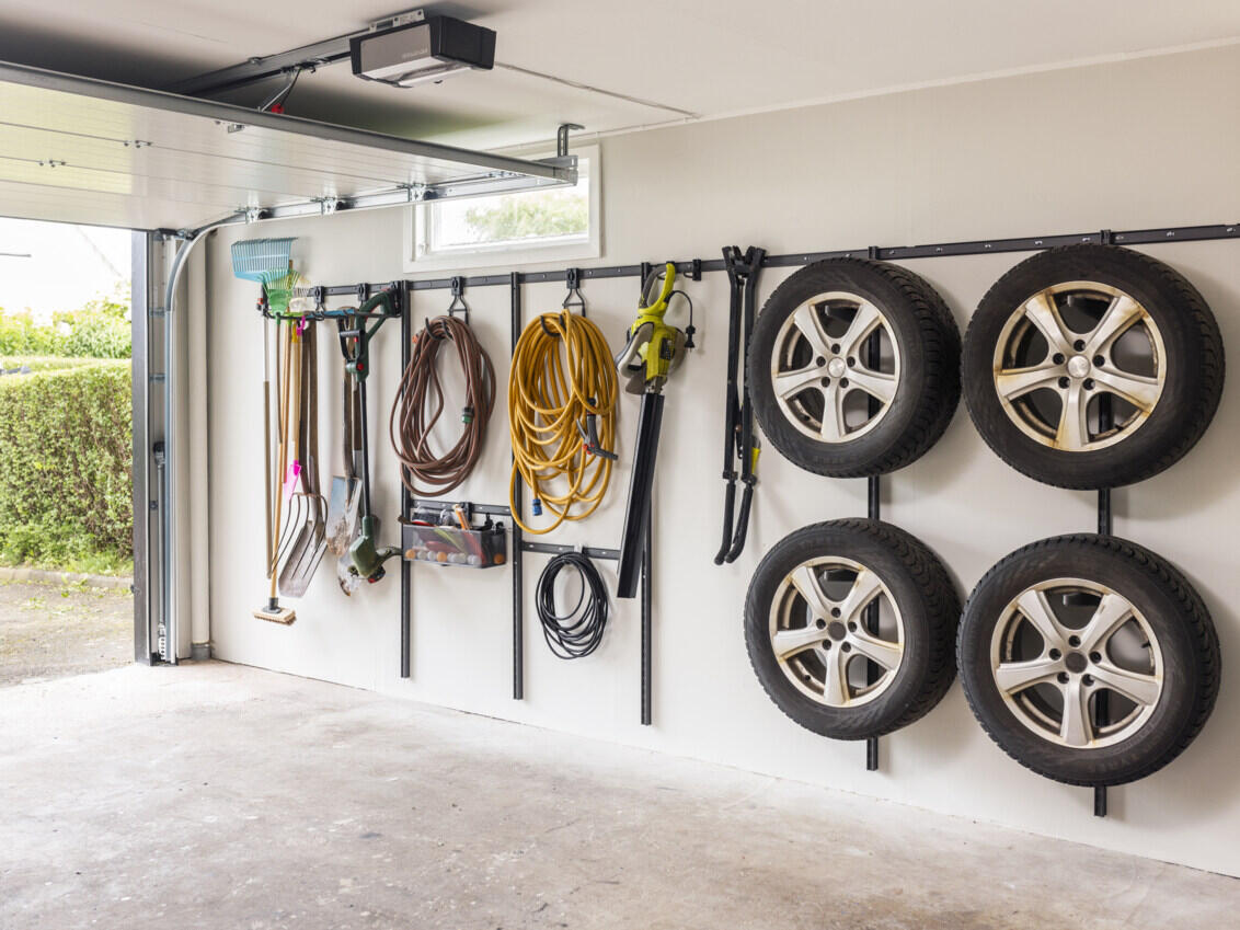 Garage med Garage+ förvaringslist från Elfa där det hänger bildäck, slangar och träddgårdsverktyg.