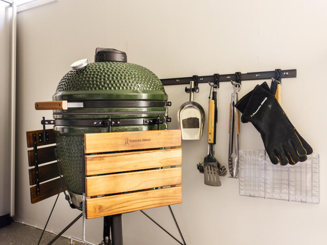 A green grill stands next to a Garage+ storage track from Elfa, where grill accessories are hanging.