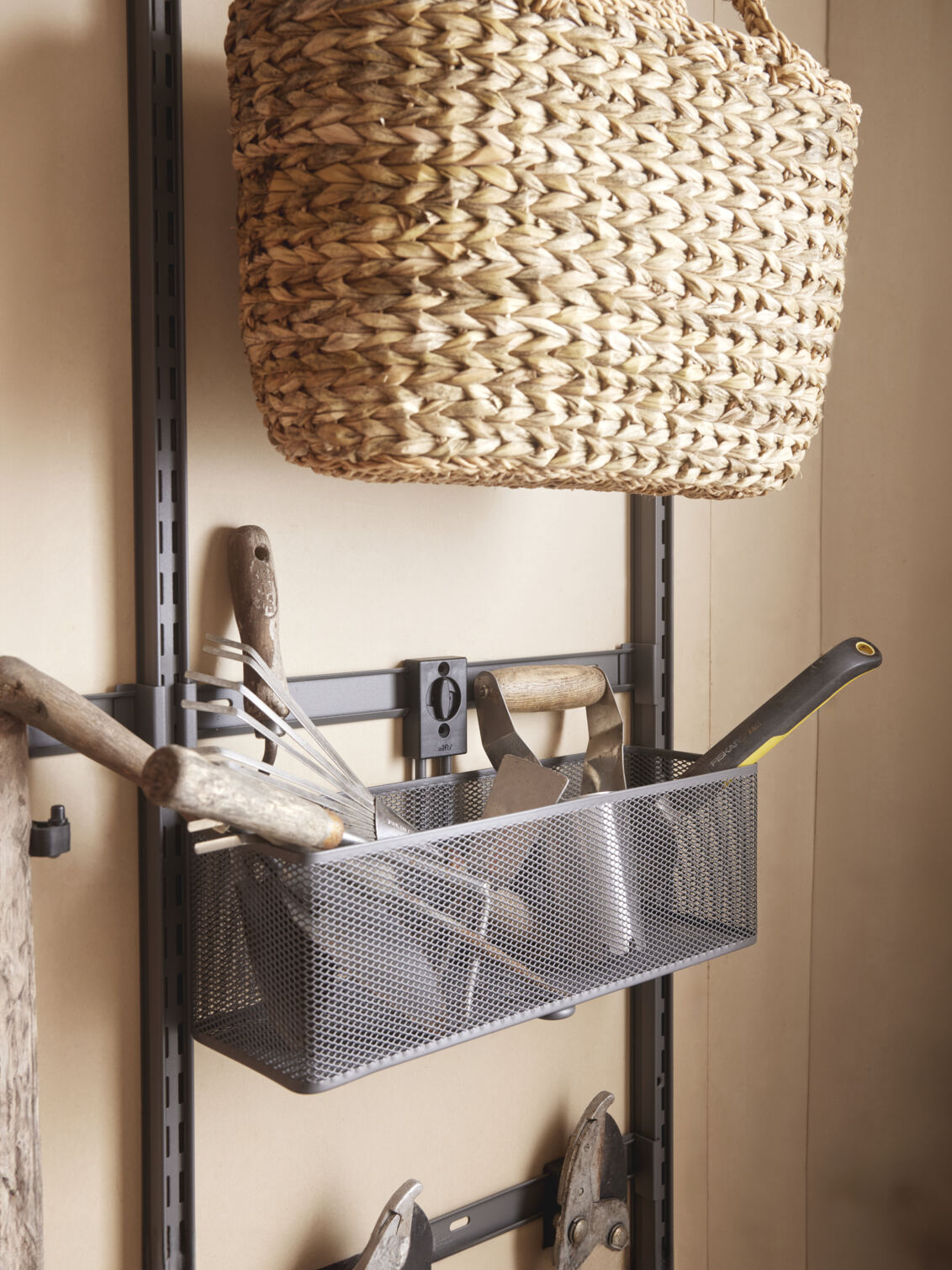 Garage+ oppbevaringslist fra Elfa der det henger en nettingkurv med hageredskaper.