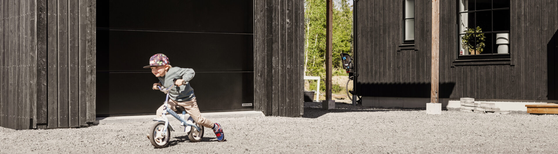 En pojke cyklar på gårdsplanen utanför ett garage.