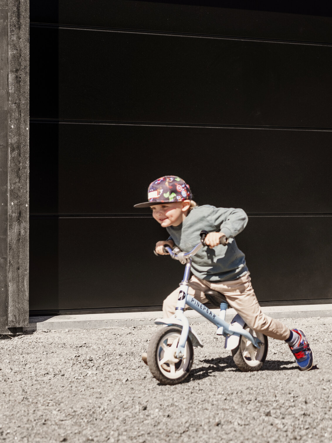 En liten pojke cyklar utanför ett garage.