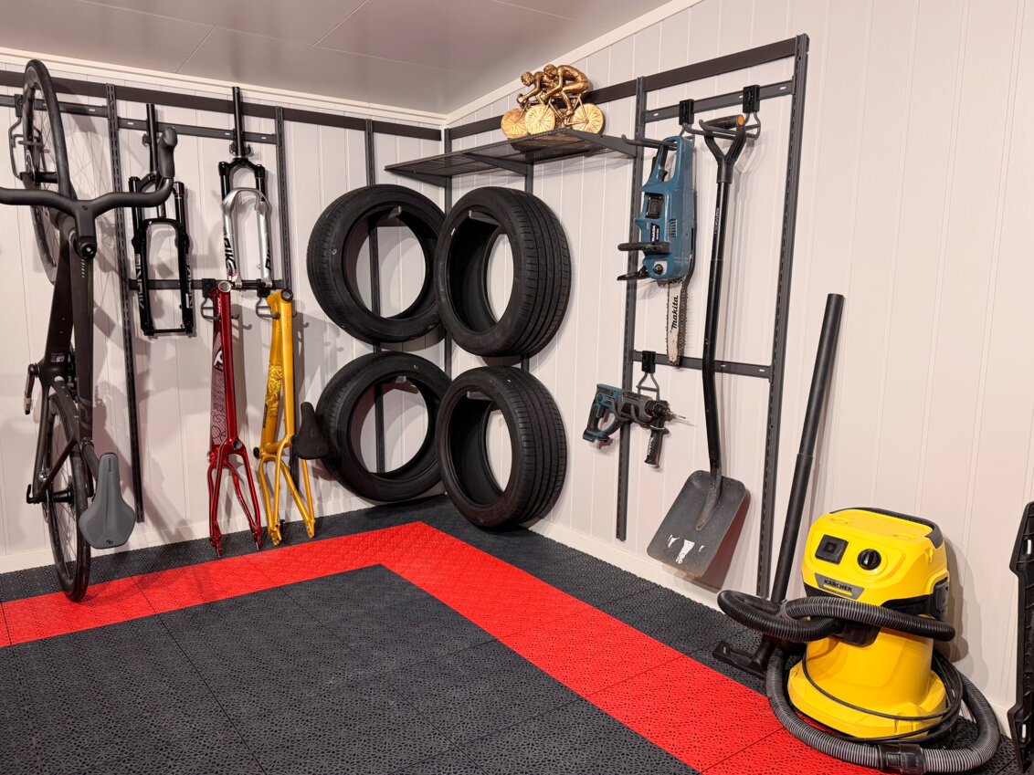 Garage med Garage+ by Elfa förvaring, där en cykel, bildäck och verktyg hänger på väggen.