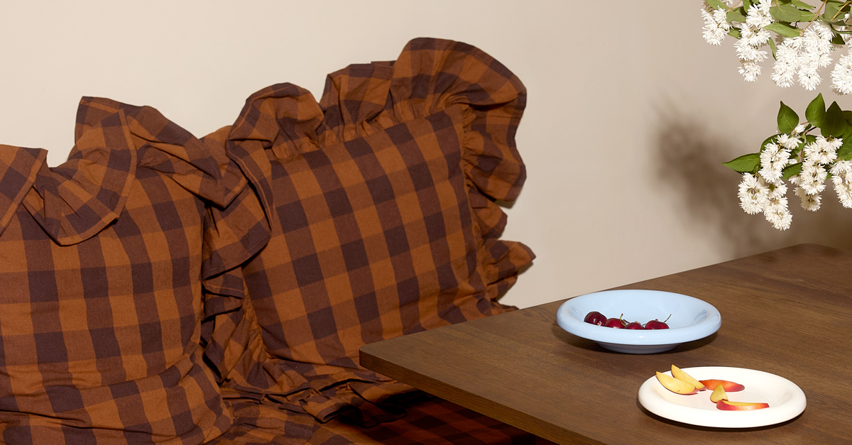 Poduszki w kratkę w kolorze brązowym przy stole z małymi talerzami, na których leżą owoce i owoce.