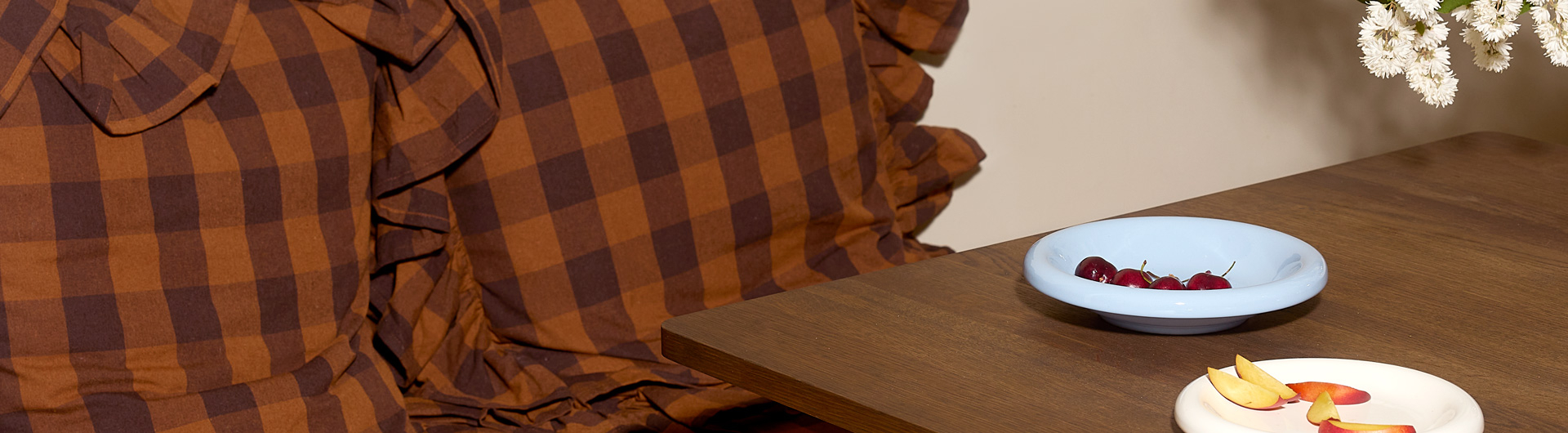 Poduszki w kratkę w kolorze brązowym przy stole z małymi talerzami, na których leżą owoce i owoce.