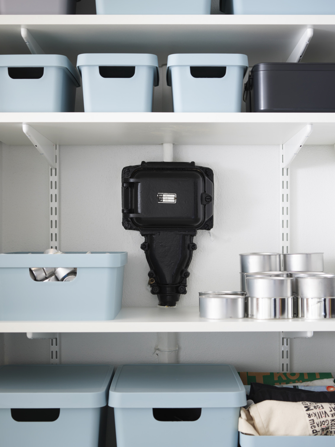 Sparring by Elfa hylla i vitt med blå förvaringslådor som är byggd runt ett elskåp.