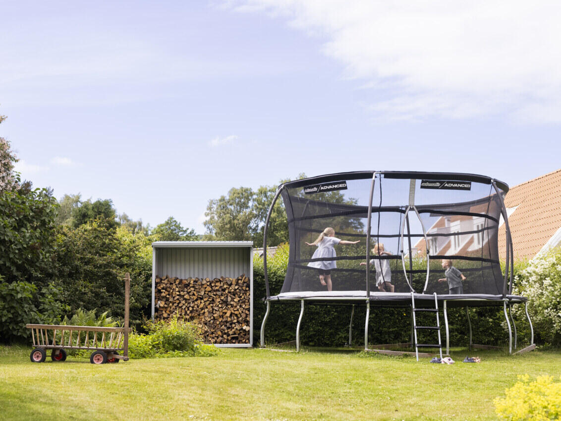 The children bounce on a trampoline in the garden next to the log shed.