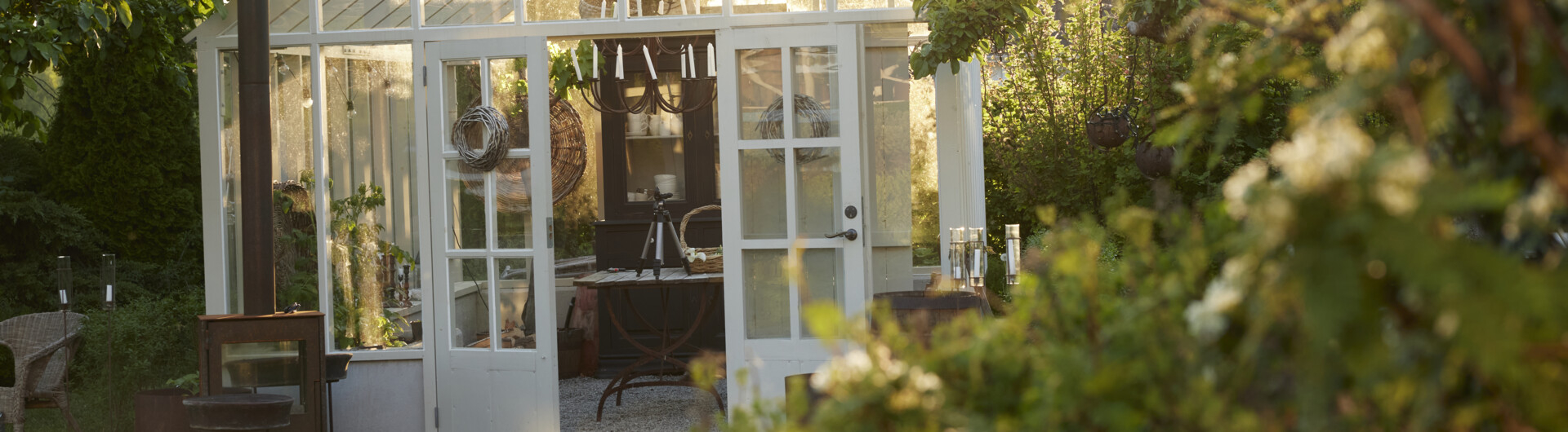 Veksthus omgitt av grønt i kveldssolen.