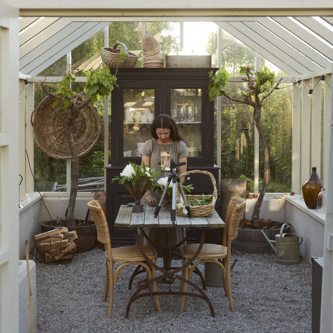 Carin takes a picture with her mobile while she arranges flowers on the garden table in her greenhouse.