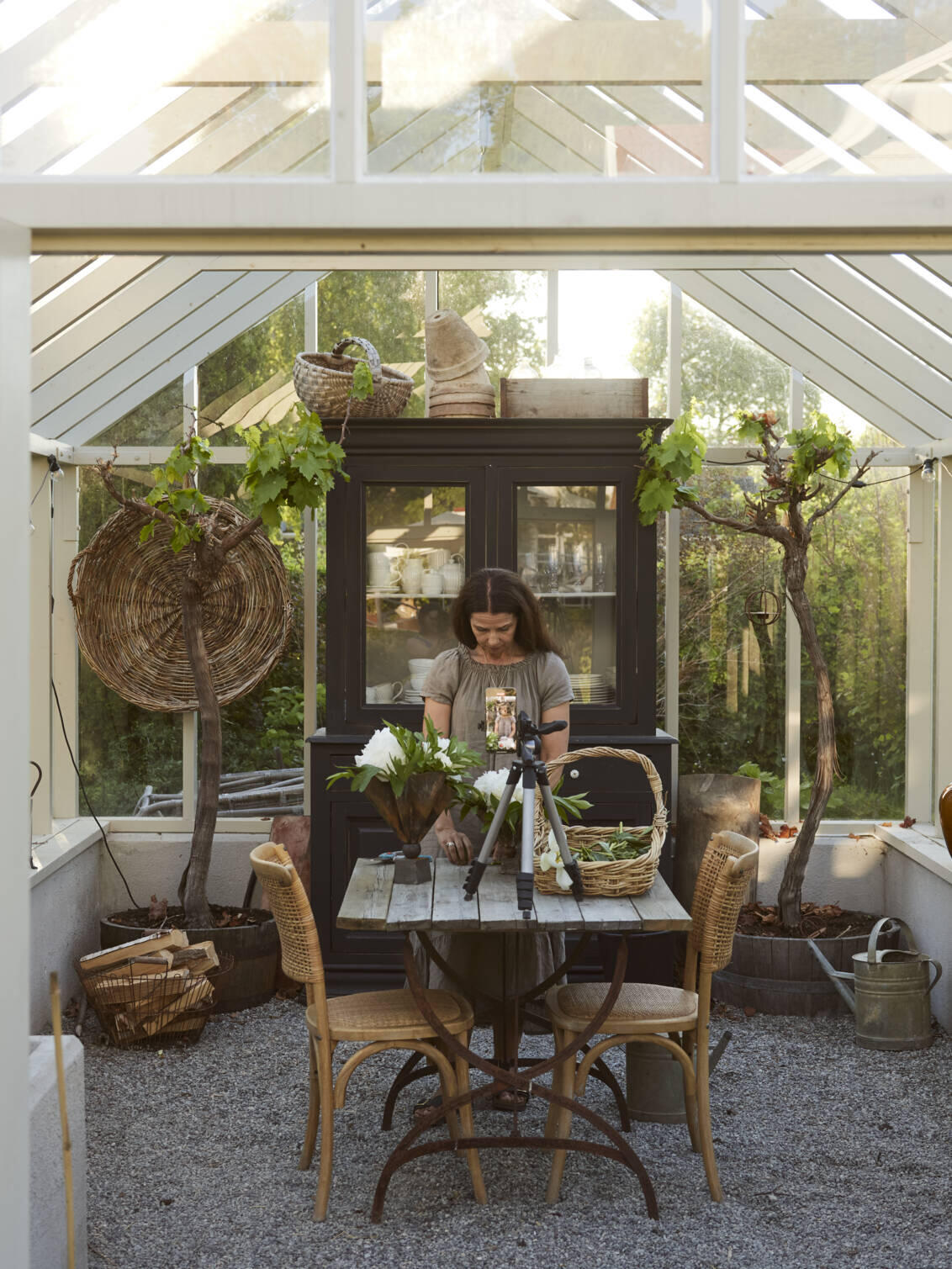 A greenhouse with a woman standing and fixing her flowers