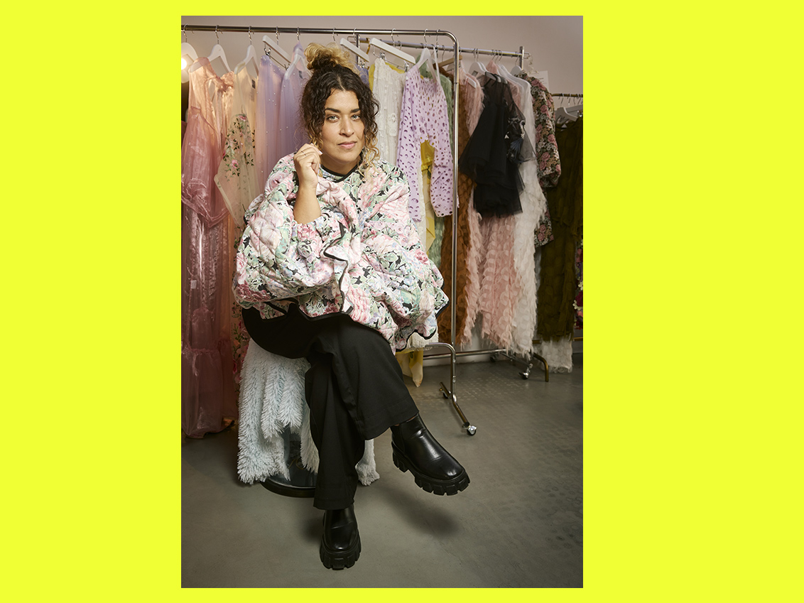 Linnea Samia Khalil sitter på en pall framför klädstänger med kläder från Pampas.