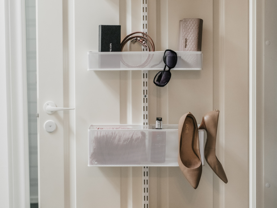 Valkoinen ovi ja Classic by Elfa -ovisäilytyskaluste, jossa on verkkokoreja, asusteita ja korkokenkiä.