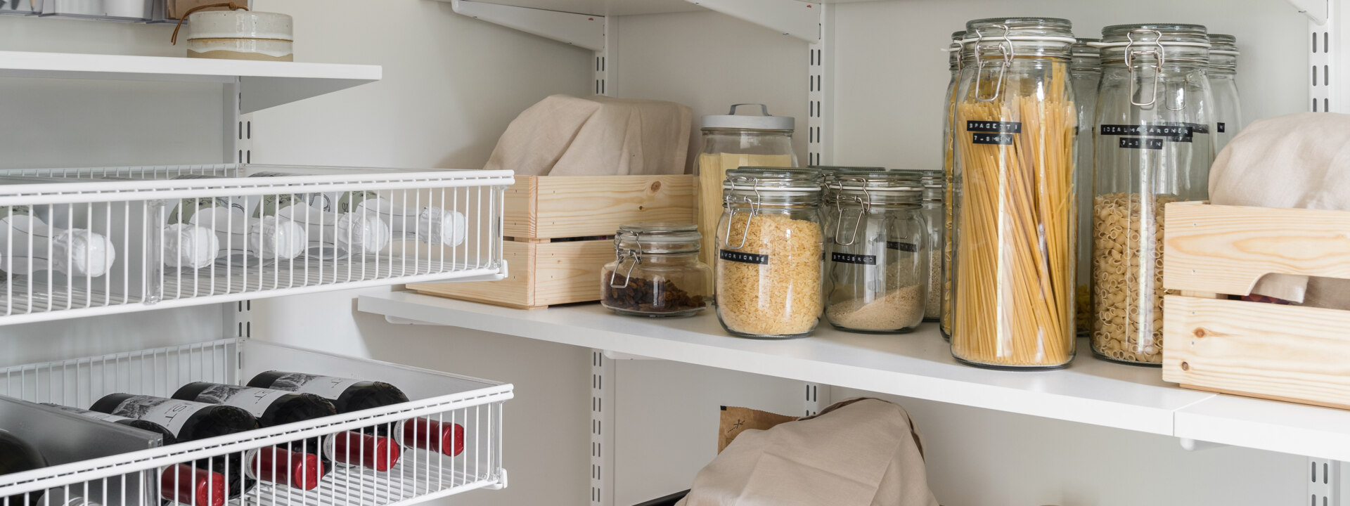 Classic by Elfa -säilytyskalusteita, joissa on hyllyillä kuivia tuotteita ja lankakoreissa viinipulloja.