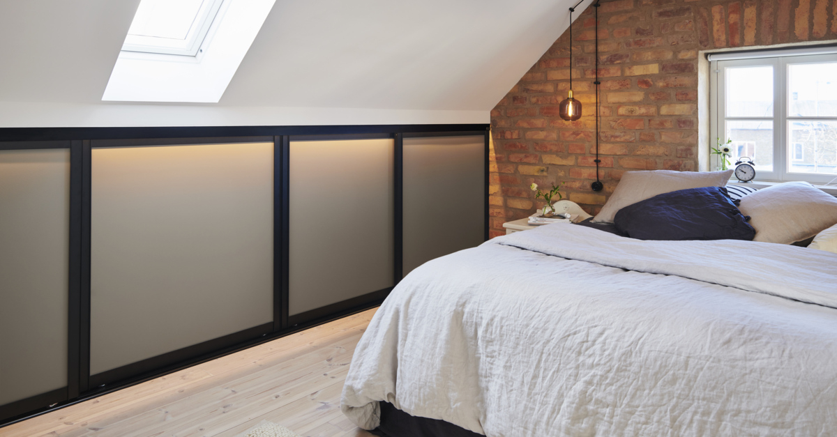 Sovrum med en låg garderob med skjutdörrar från Elfa under snedtaket.