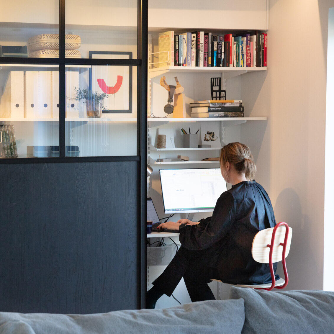 A woman is sitting in a home office with sliding doors from Elfa in black and glass.