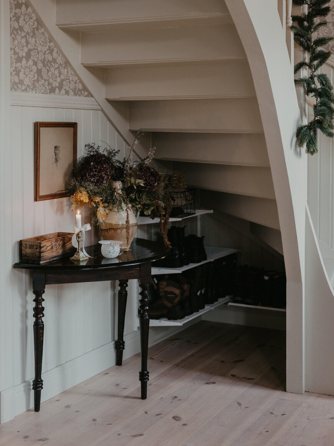 Utrymme under en trappa med skohyllor från Classic by Elfa i vitt samt ett bord med dekorationer på.