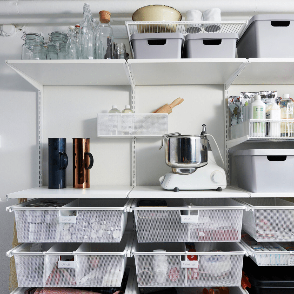 Klassisk hengeoppbevaring fra Elfa med hyller og nettingbrett fylt med stearinlys, servietter og snorer.