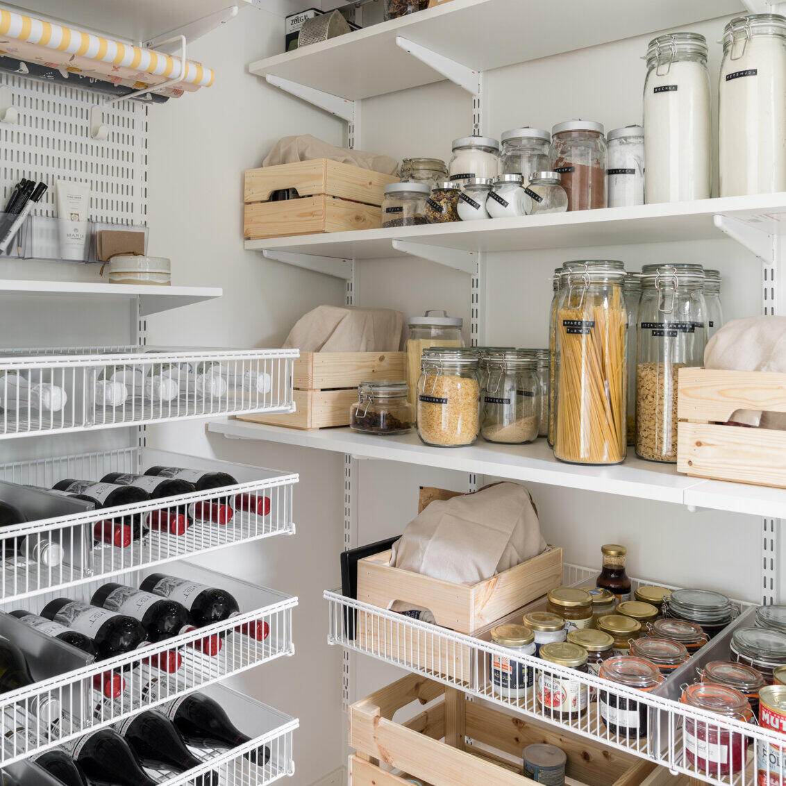 Classic by Elfa -säilytyskalusteita, joissa on hyllyillä kuivia tuotteita ja lankakoreissa viinipulloja.