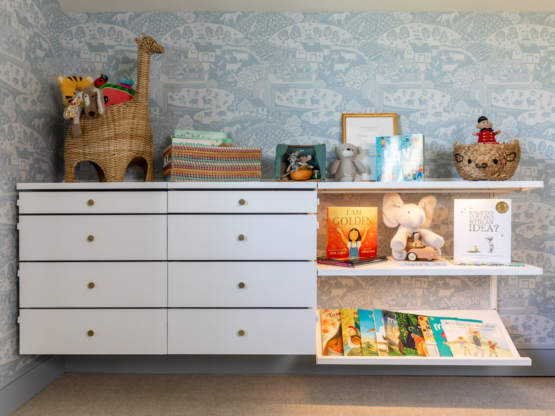 Pokój dziecięcy z systemem przechowywania Décor+ by Elfa z wysuwanymi szufladami i białymi półkami pełnymi zabawek i książek.