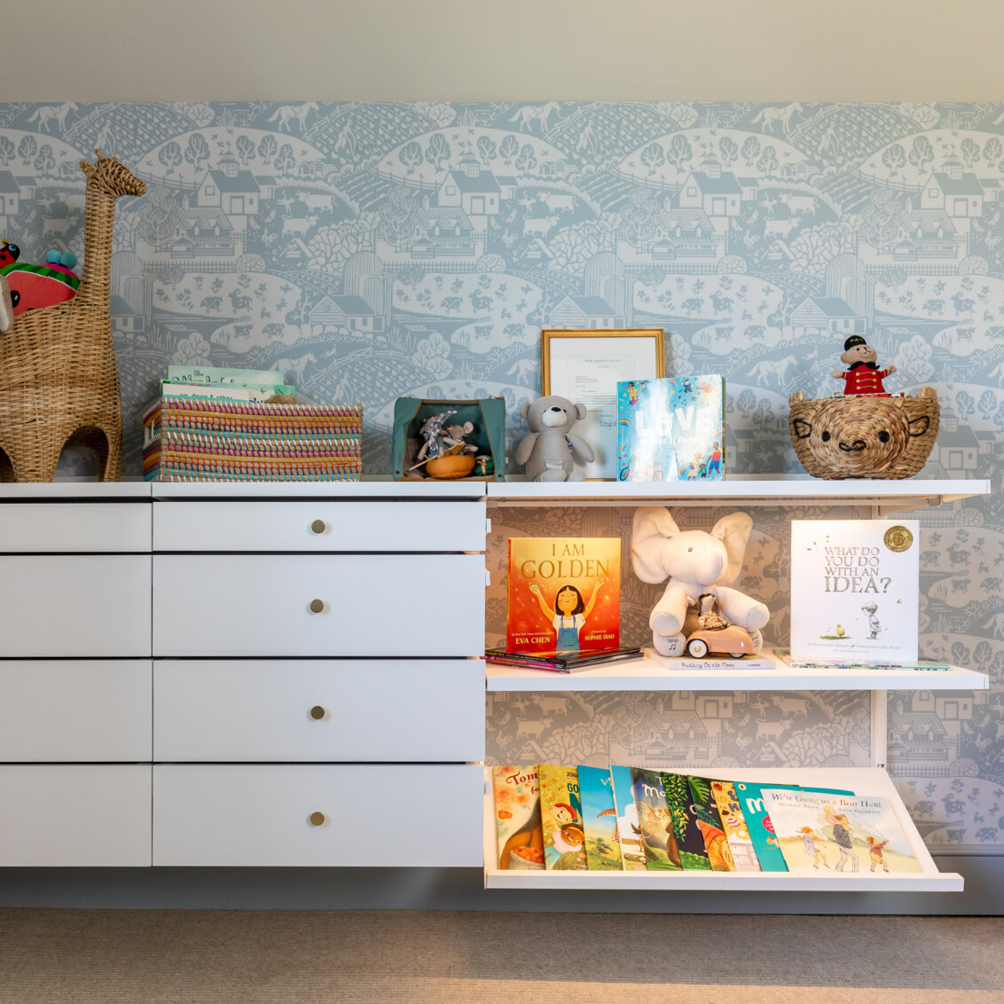 Pokój dziecięcy z systemem przechowywania Décor+ by Elfa z wysuwanymi szufladami i białymi półkami pełnymi zabawek i książek.
