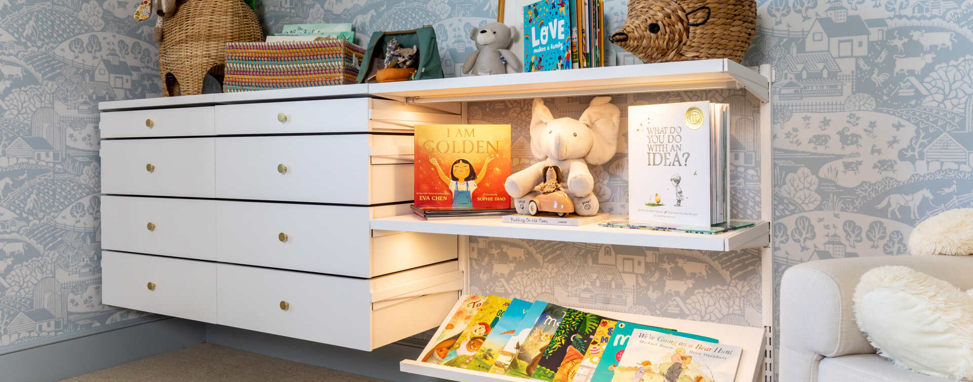 Pokój dziecięcy z systemem przechowywania Décor+ by Elfa z wysuwanymi szufladami i białymi półkami pełnymi zabawek i książek.
