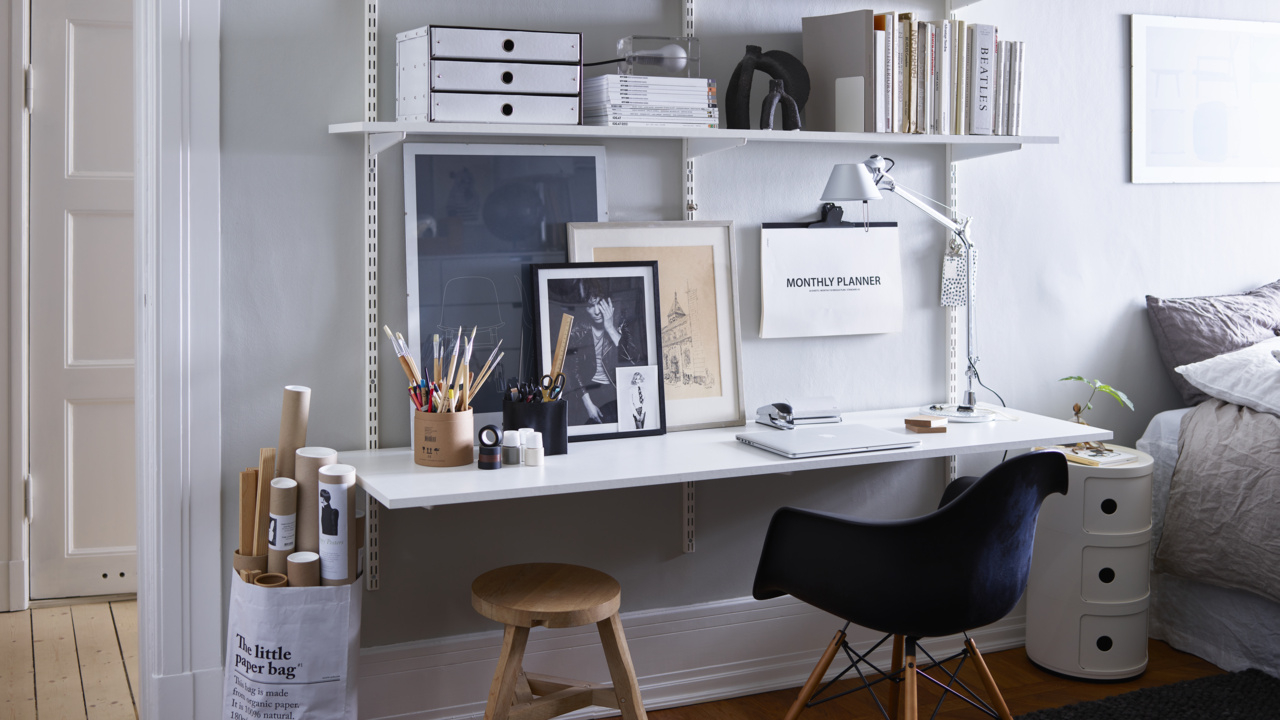 Kotitoimisto, jossa on Elfan perinteinen seinälle asennettava Sparring-hyllyjärjestelmä, musta toimistotuoli ja puujakkara.