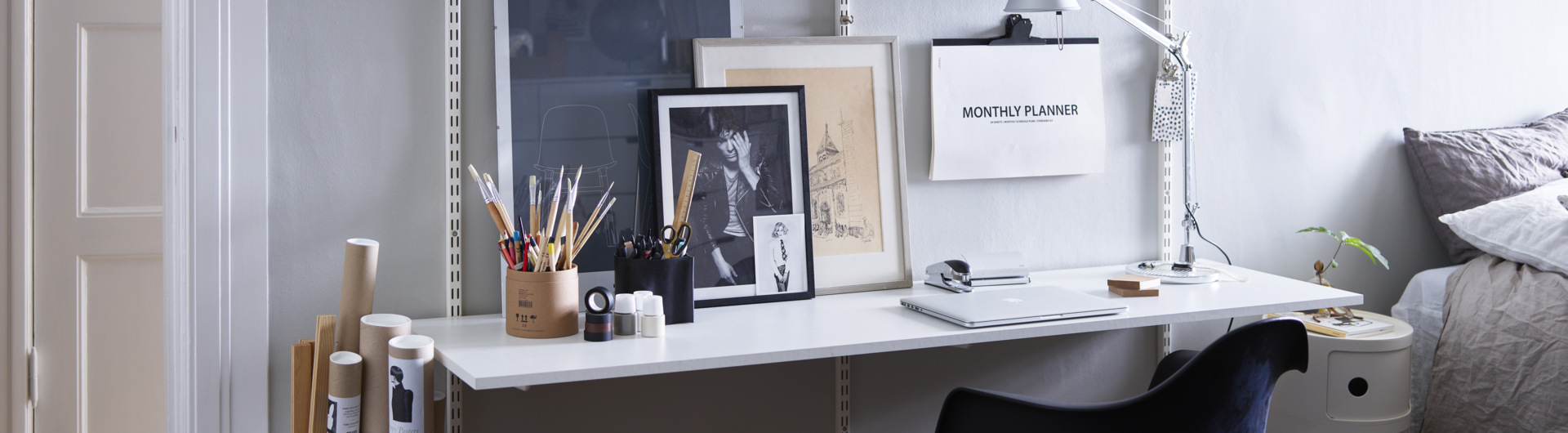 Kotitoimisto, jossa on Elfan perinteinen seinälle asennettava Sparring-hyllyjärjestelmä, musta toimistotuoli ja puujakkara.