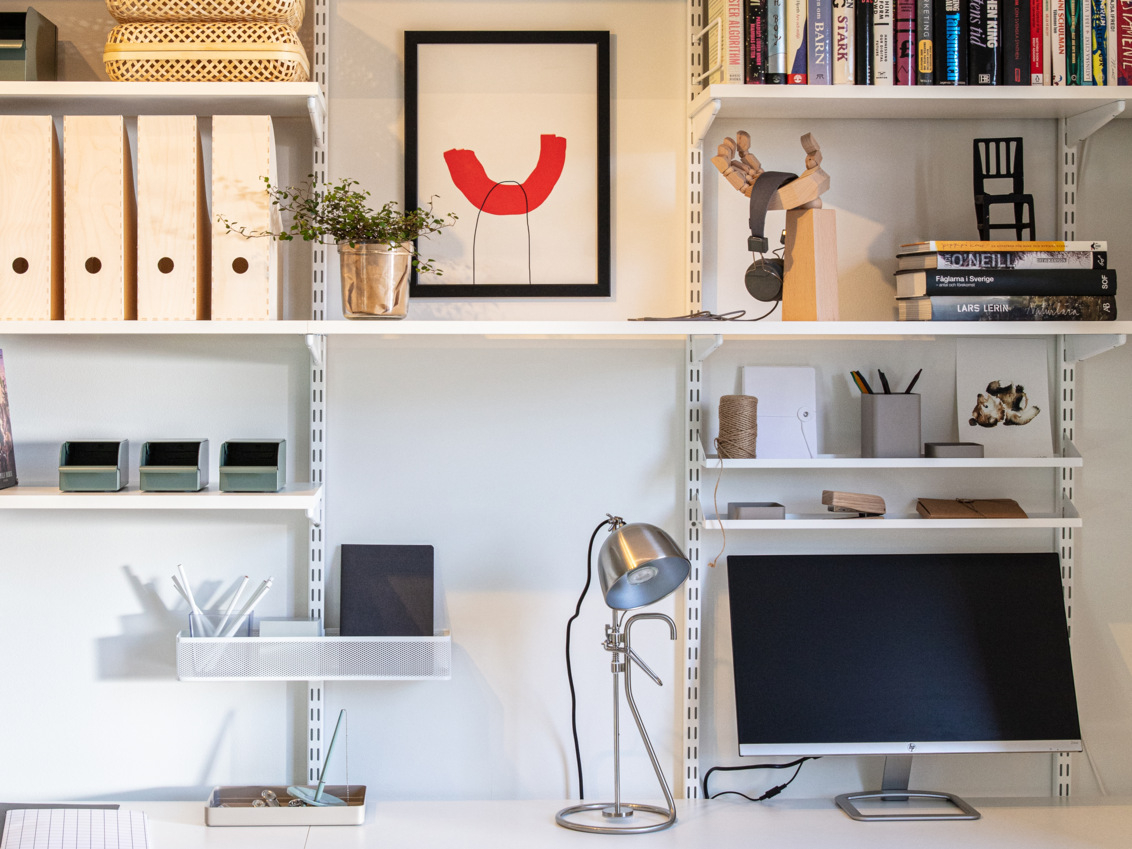 Kotitoimisto, jossa on valkoinen Classic by Elfa -säilytyskaluste, jossa henkilökohtaisia yksityiskohtia säilytetään eri syvyisillä hyllyillä.